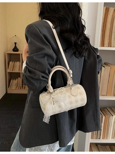 Sac cylindrique à damier crème avec nœud en dentelle porté par un mannequin