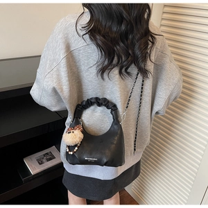 Detail der schwarzen Handtasche mit Rüschengriff, Kettenriemen und Bärenanhänger-Accessoire