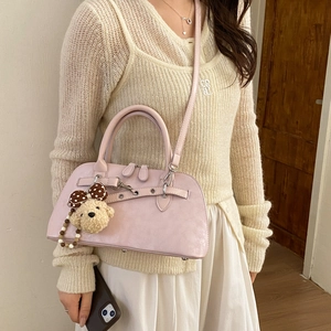 Side view of pale pink matte leather crossbody bag with teddy bear charm on model