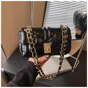 Detail of black quilted chain strap bag with golden twist lock and textured leather