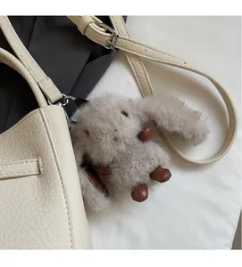 Dettaglio di un ciondolo a coniglio grigio soffice su una borsa in pelle beige martellata