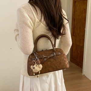 Detail of retro dark brown leather boston bag with metal buckle and teddy bear charm