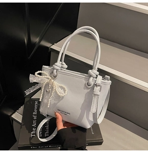Détail d'un sac seau bleu clair avec perle décorative et nœud en dentelle sur la poignée