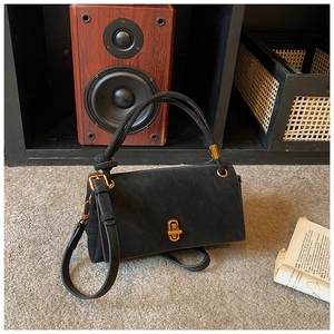 Detail of matte black rectangle handbag with retro gold twist lock on plush carpet