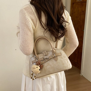 Detail of beige textured leather handbag featuring a plush bear charm and bow decoration