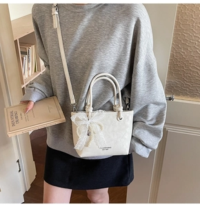 Détail du sac seau crème avec nœud en dentelle et chaîne de perles décorative