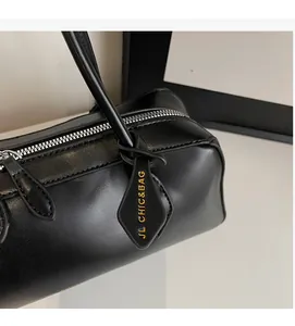 Détail d'un sac cylindrique en cuir noir avec zip argenté et étiquette logo dorée chic