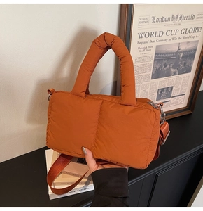 Detail of orange quilted puffer bag showing wide padded handle and detachable strap