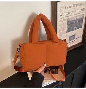 Close-up of orange quilted down tote bag featuring padded handles and detachable strap