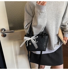 Détail du sac seau noir avec nœud en dentelle blanche et pendentif en perle