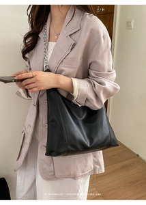 Detail of black tote bag featuring a chunky silver metal chain strap and sleek leather