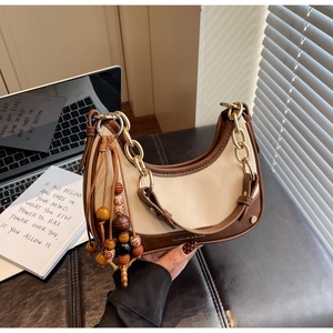 Detail of two-tone croissant bag with gold chain strap and wooden bead tassel decor