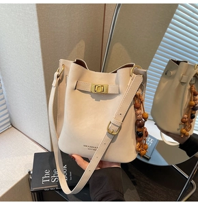 Detail of cream leather bucket bag with gold twist lock and wooden bead tassel ornament