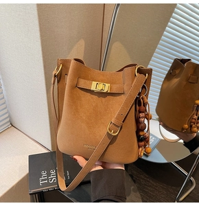Detail of a brown frosted suede bucket bag with gold twist lock and beaded charm