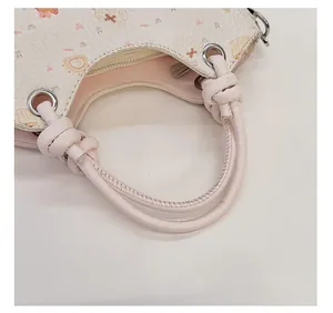 Close-up of a pink knotted leather handle on a cream handbag with cartoon prints