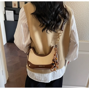 Detailed view of bicolor chain square bag with wooden bead tassel on female model