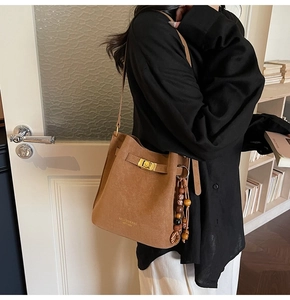 Close-up of brown suede bucket bag featuring ethnic style wooden bead charm and gold lock