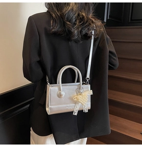 Detail of silver crossbody bag with pearl bow and lace trim on a black blazer