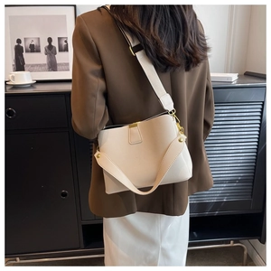 Gros plan sur le sac seau en cuir beige avec finitions dorées et bandoulière en tissu