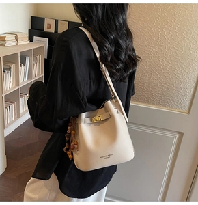 Close-up of cream leather bucket bag with gold clasp and wooden bead charm detail