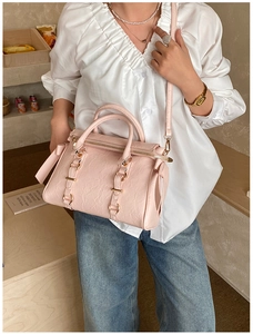 Pink pleated leather Boston bag with gold hardware shown as a crossbody in a cozy setting