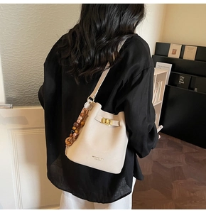 Detail of a beige leather bucket bag with gold twist lock and colorful beaded charm