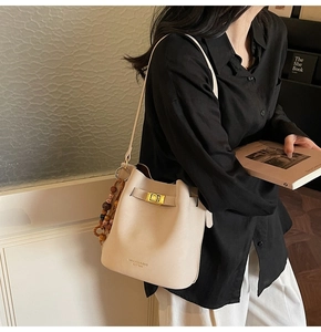 Detail of cream bucket bag featuring a gold clasp and colorful wooden bead charms