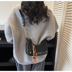 Detail of black leather hobo bag featuring gold chain strap and wooden bead tassel