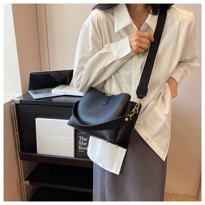 Détail du sac seau en cuir noir grainé avec large bandoulière et boucle en métal doré