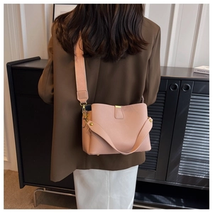Sac seau en cuir rose pâle avec large bandoulière porté par un mannequin en tailleur
