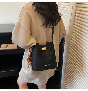 Detail view of black bucket bag with gold metal lock and vintage wooden bead charm
