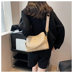 Sac seau en cuir beige grainé porté par un mannequin avec bandoulière large et pieds en métal