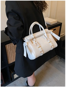 Detailed texture of white leather tote bag with gold hardware worn with black suit