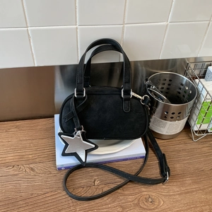 Close-up of black suede Boston bag with star charm on a wooden table setting
