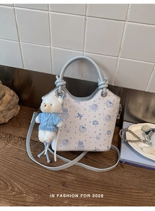 Detail of light blue crossbody bag with bear print and cute plush charm on wood table