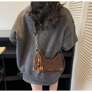 Détail du sac demi-lune marron foncé avec chaîne dorée et gland en perles de bois