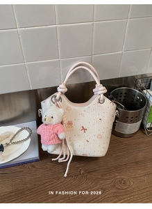 Close-up of white leather bucket bag with pink ribbon handle and plush bear charm accessory