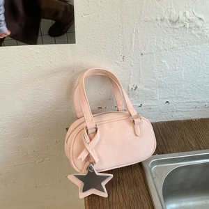 Close-up of pink Boston bag with ribbon bow and star mirror charm on wooden surface
