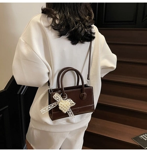 Deep brown crossbody tote bag with pearl heart charm and lace bow on retro wood stairs