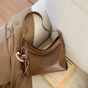 Brown vintage faux leather tote bag with brand logo and wooden horse charm on a sofa