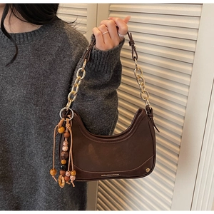 Detail of brown half-moon bag with gold logo, chunky metal chain and beaded tassel