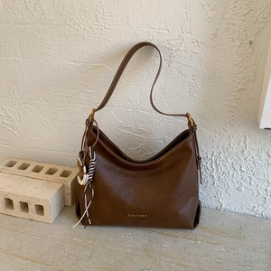 Detail view of a dark brown retro moon bag with gold hardware and logo on stone base
