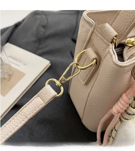 Détail macro du sac seau en cuir beige avec crochets dorés et pendentif tissé