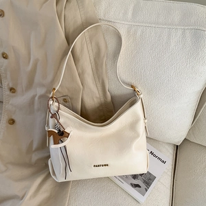 Detail of cream white faux leather tote bag with metal logo and horse charm on sofa