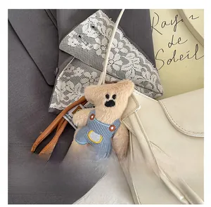 Detail of a cute plush bear charm in blue overalls hanging on a white crossbody bag