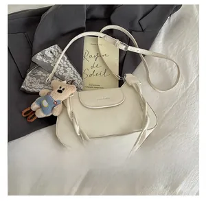 Detail view of cream PU leather handbag with woven handle and blue teddy bear charm