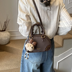 Sac Boston marron avec breloque ours et bandoulière porté par un mannequin décontracté