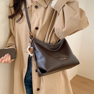 Detail of dark brown faux leather tote with gold logo and horse charm on beige coat