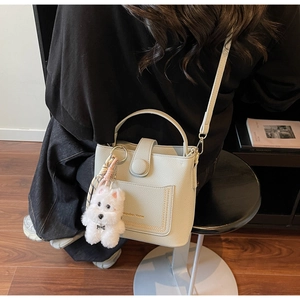 Détail du sac seau beige grainé avec lettrage doré et breloque chien en peluche