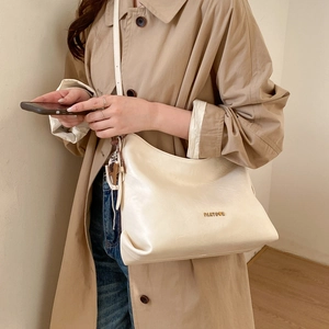 Close-up of a large beige leather tote bag with gold metal logo on a neutral trench coat